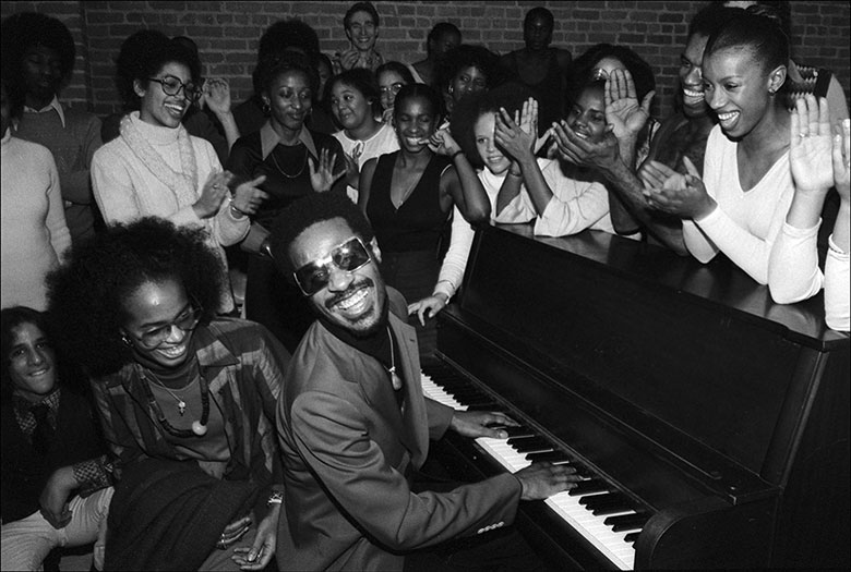 Stevie Wonder sitting at a piano entertaining students at the Dance Theater of Harlem in New York